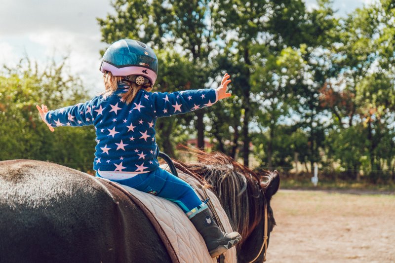 Kleines Kind sitzt freihändig auf dem Pferd, hinter einem Voltigiergurt